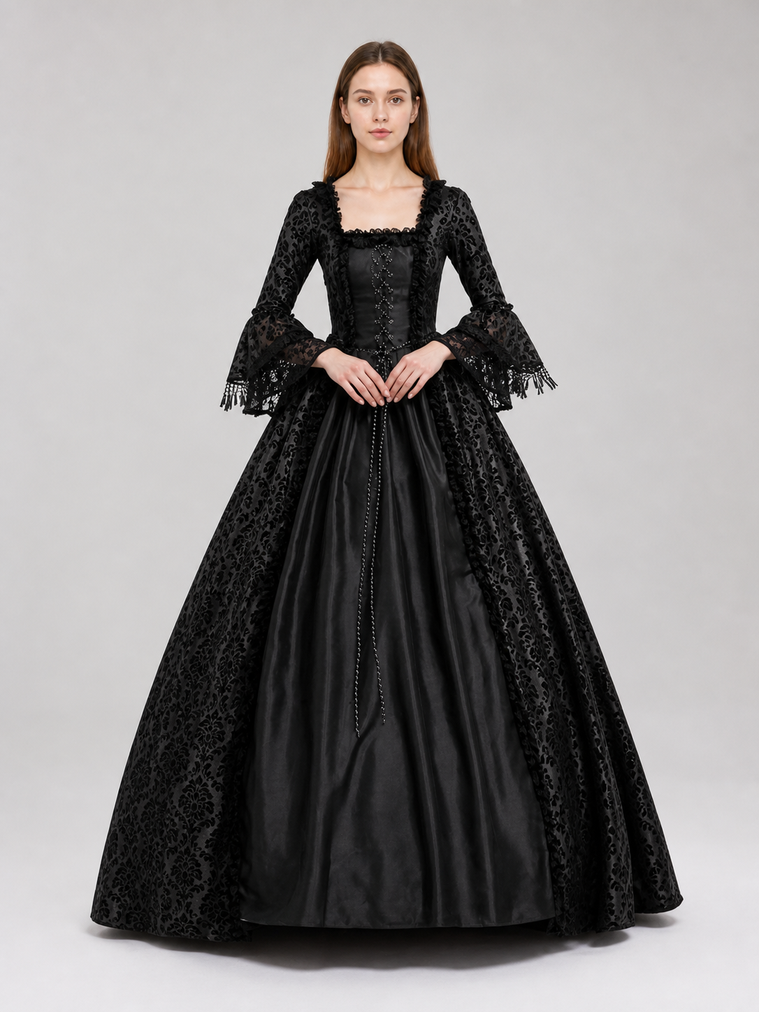 The black dress is designed in the aesthetic of a Victorian-era Gothic costume. The model features a floor-length silhouette, a fitted bodice with a square neckline, and decorative lacing or trim on the front. The long flared sleeves end in