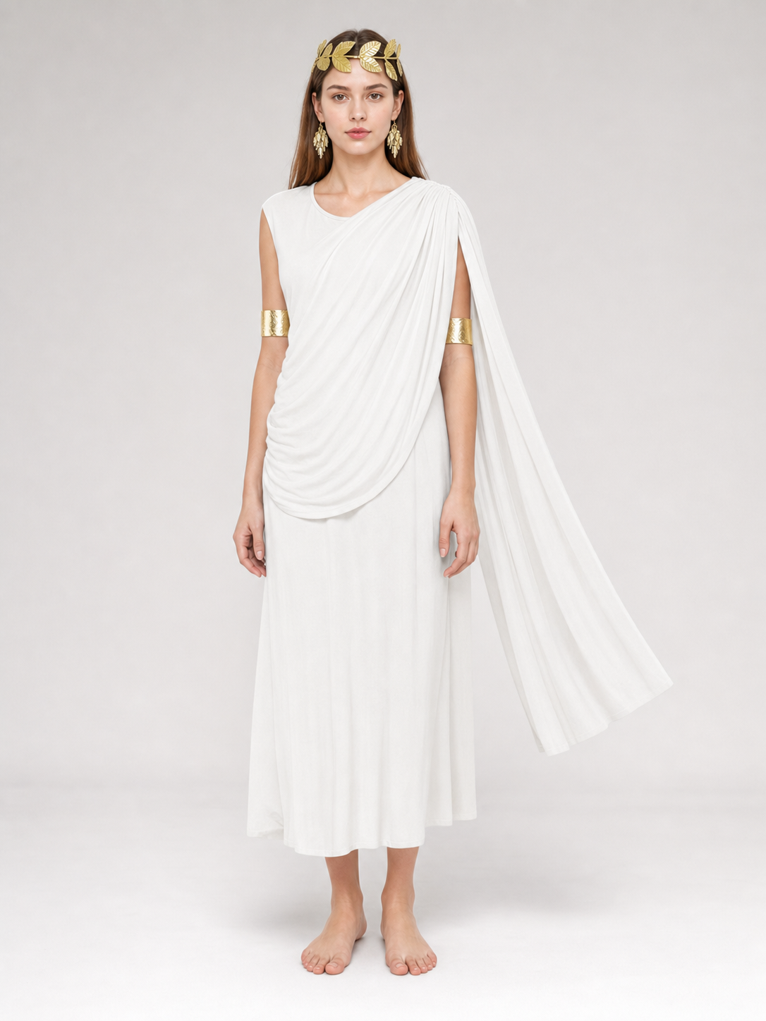 Full-body model wearing a white draped dress with a long train and gold arm bands, barefoot against a plain gray background