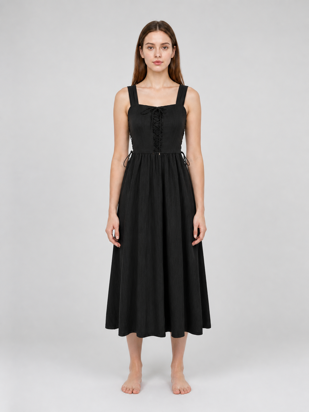 Black midi dress shown full-body from the front on a model, with wide straps, center lacing, side ties, and a softly gathered skirt