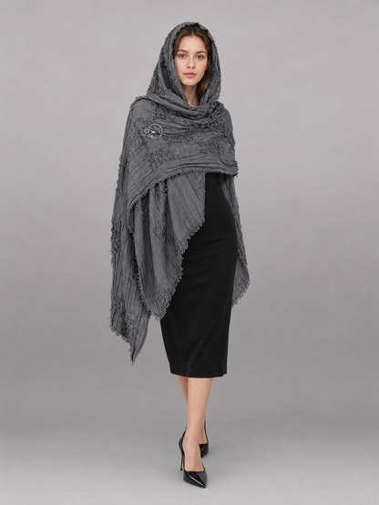 This large scarf-wrap is designed as a rectangular drape with a striking textured surface. The black-and-gray color palette is accented with lighter gray tones, giving the piece a distinctive look that pairs easily with different outfits. T