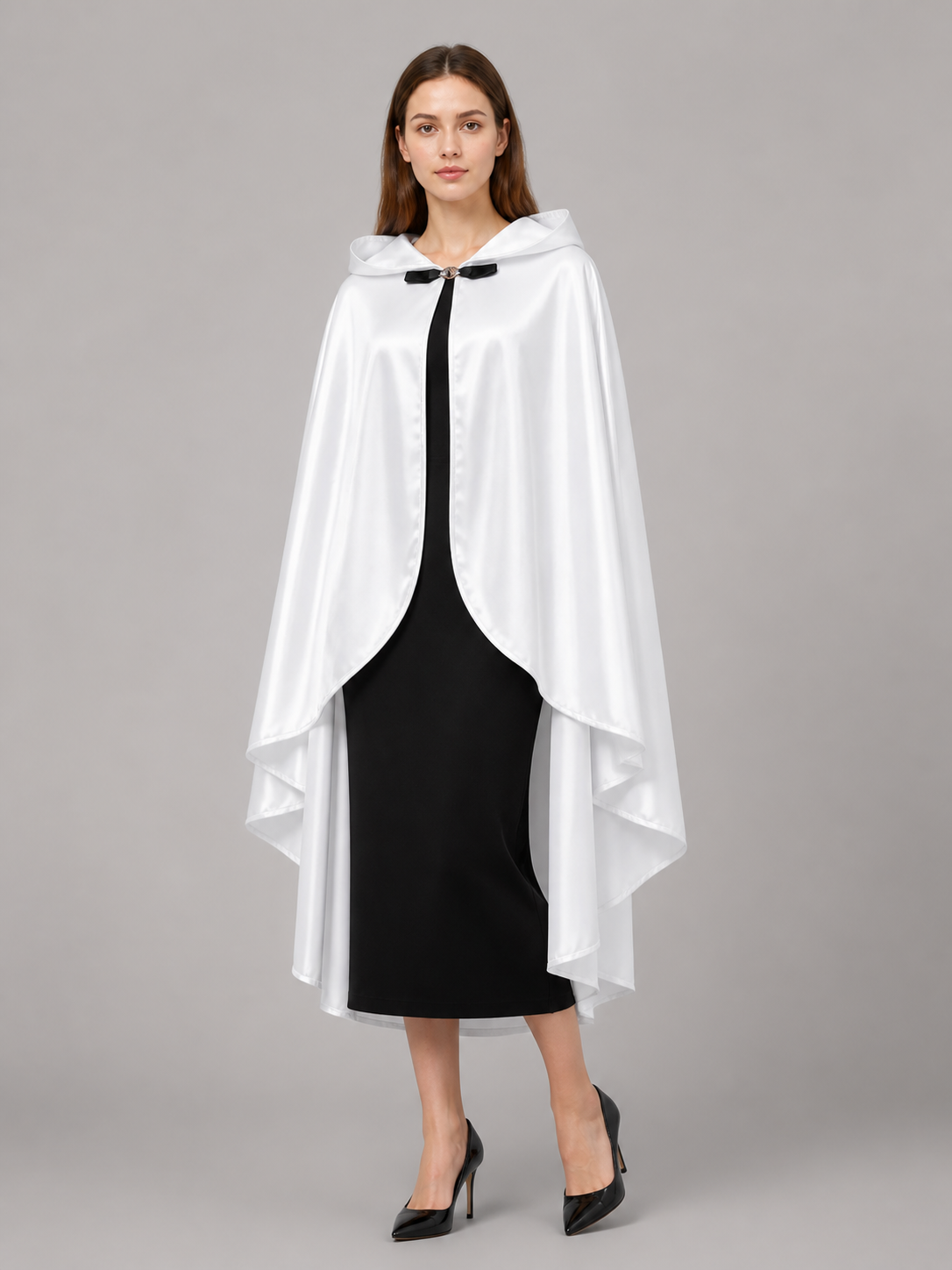 White hooded cape with glossy fabric, curved front opening, and layered hem, shown on a model in a black dress and heels