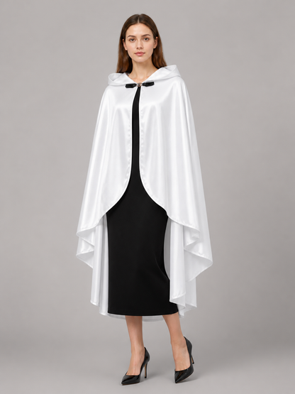 White hooded cape with glossy fabric, curved front opening, and layered hem, shown on a model in a black dress and heels