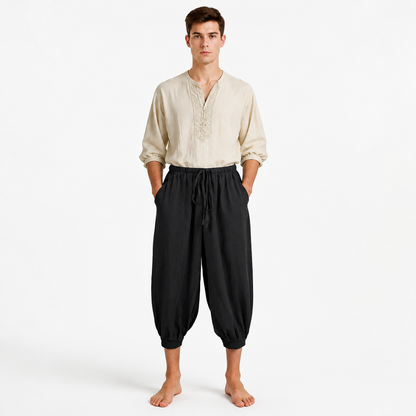 Full-body front view of a man wearing black cropped harem pants with a gathered waistband, drawstring, pockets, and ankle cuffs