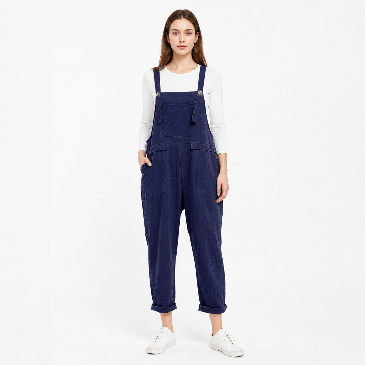 Front view of navy blue bib overalls on a model wearing a white long-sleeve shirt, with metal strap buttons and large front pockets