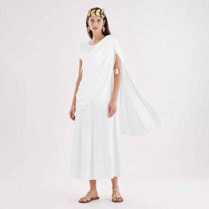 Three-quarter model view of a white draped dress with a shoulder train, gold arm bands and flat sandals against a plain background