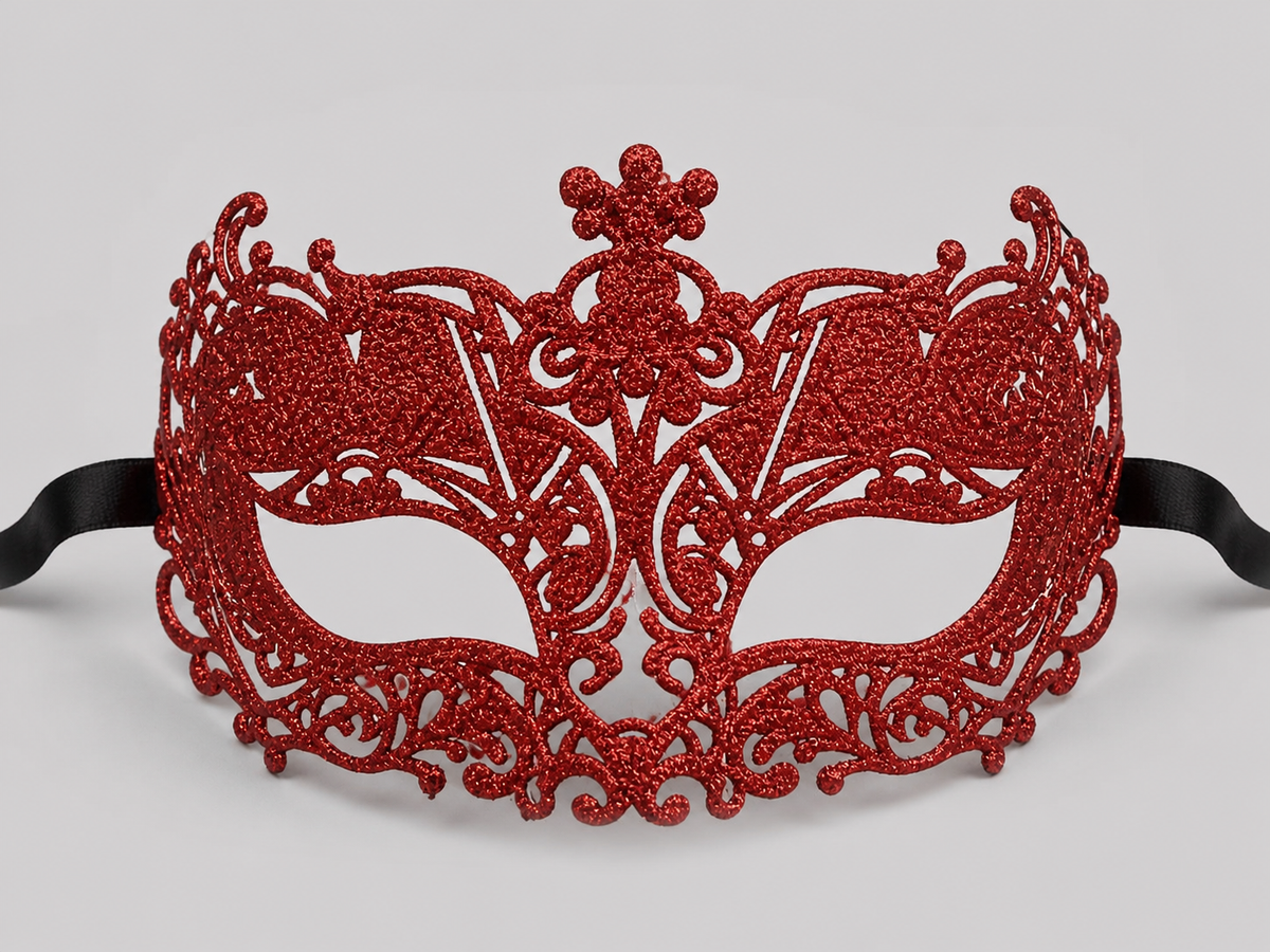 Red glitter openwork masquerade mask with ornate scrollwork, eye openings, and black ribbon on a gray background