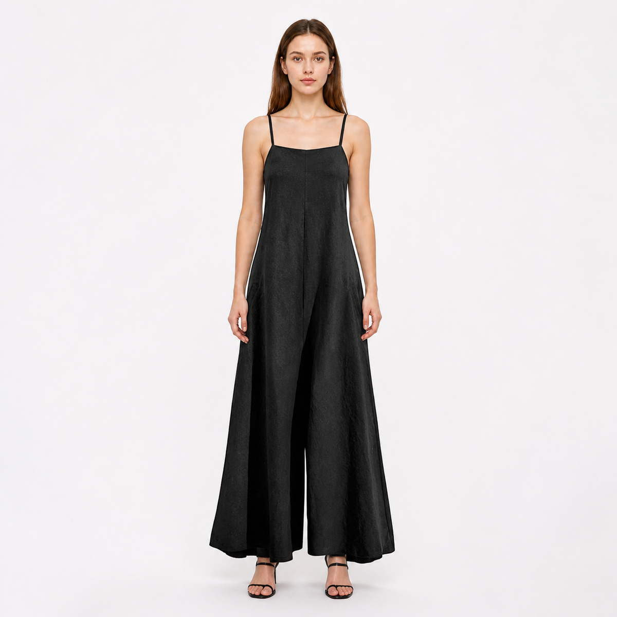 Front view of a black wide-leg jumpsuit with thin straps, modeled full-body against a light studio background with black sandals