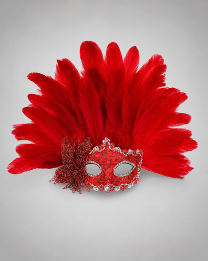 Red feather masquerade mask displayed upright on a gray surface, with a glittered eye mask, silver edging, and side bow