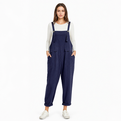 Full-body front view of navy blue bib overalls over a white shirt, showing adjustable shoulder straps, front pockets, and rolled cuffs