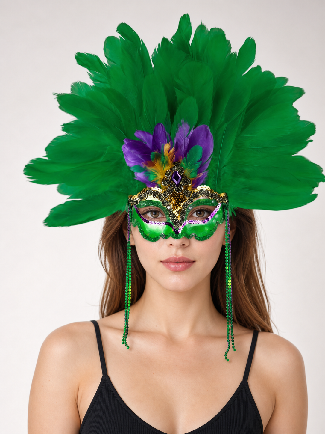 Close-up front view of a woman wearing a green feather eye mask with purple feathers, gold trim, and dangling side strands