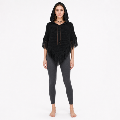 Black hooded knit poncho with pointed fringed hem, shown full-body on a barefoot model against a light background