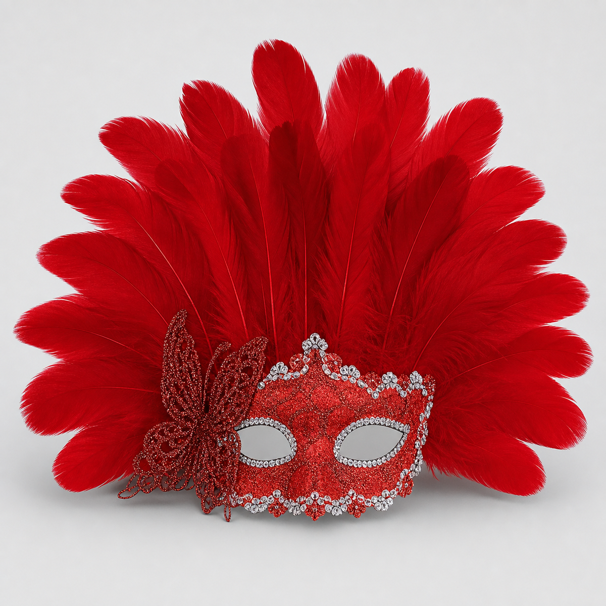 Close-up of a red feather mask showing layered plumes, glittered red eye covering, silver rhinestone edging, and side bow