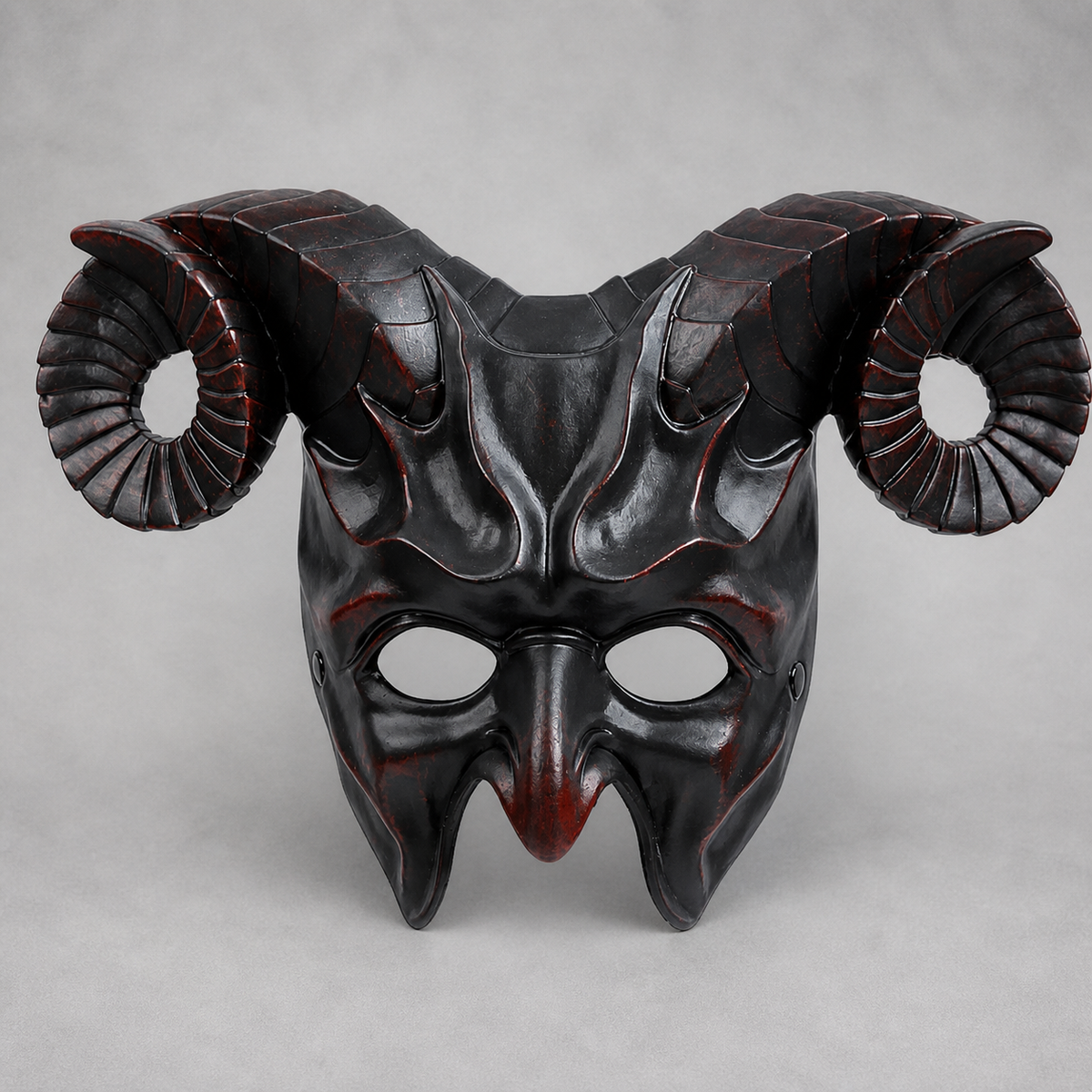 Glossy black horned mask displayed upright against a gray background, with curled ridged horns, eye openings, and pointed details