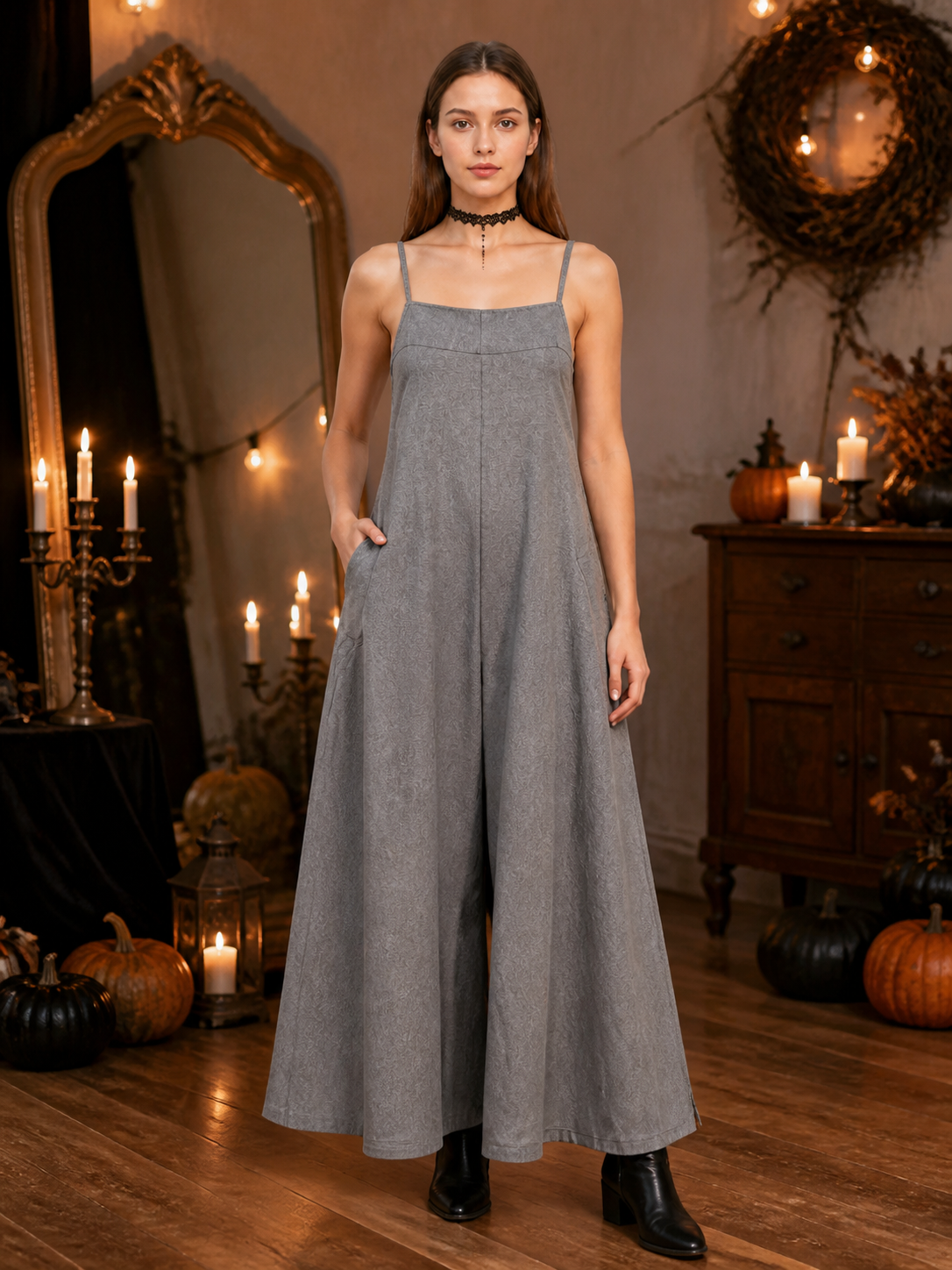 Gray wide-leg jumpsuit with thin straps and side pockets, shown full-length on a model in a candlelit room