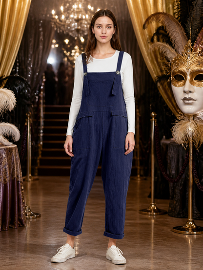 Front view of navy blue bib overalls over a white long-sleeve shirt, styled with white sneakers in an ornate indoor setting