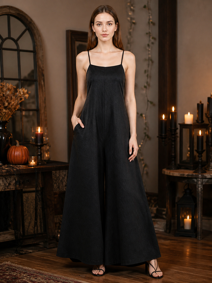 Black wide-leg jumpsuit with thin straps and a side pocket, modeled in a candlelit room with pumpkins and lanterns