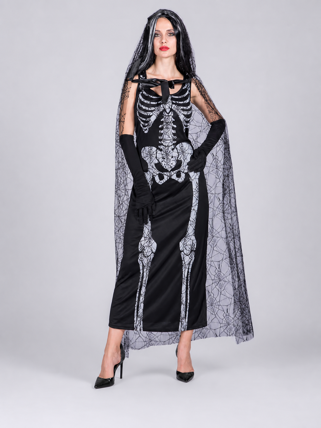 Gothic Halloween costume dress with accessories: a sleeveless black dress with a white rib and pelvic bone print, a sheer cape or veil with a spiderweb design, black gloves, and a necktie or bow detail. The look is done in black and white w