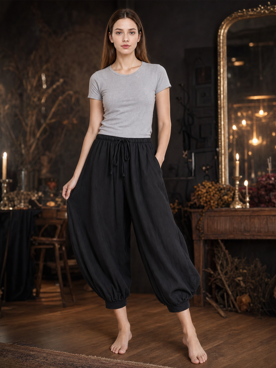 Woman wearing black cropped harem pants with side pockets and a drawstring waist, posed in a dim room with candles and a mirror