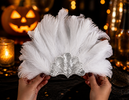 White feather headband held in both hands in a dim festive setting, with a silver sequined front and decorative lights