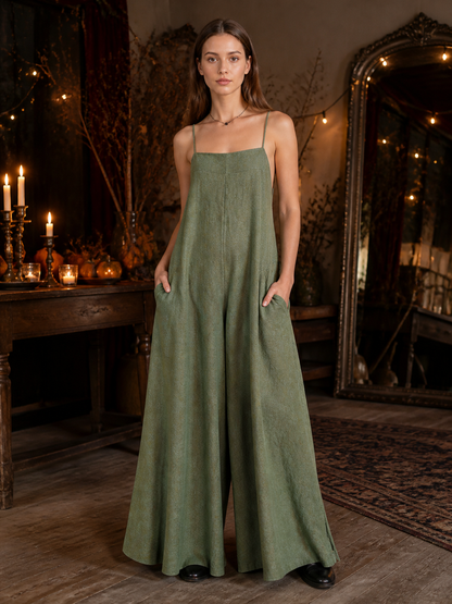 Olive green wide-leg jumpsuit with thin straps and side pockets, shown full-body on a model in a candlelit room