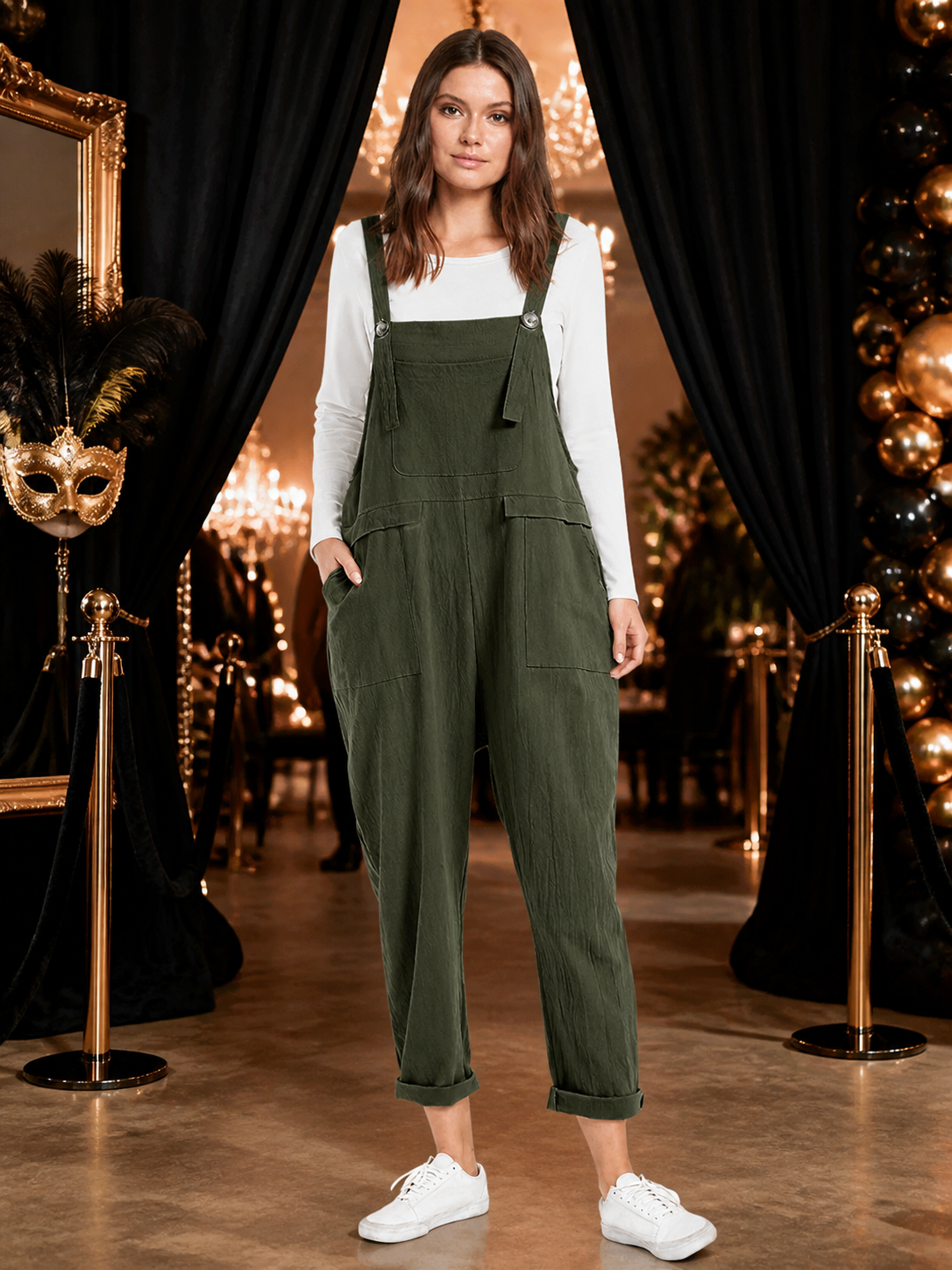 Full-body model wearing dark green bib overalls with a chest pocket and side pockets in a black-and-gold decorated interior