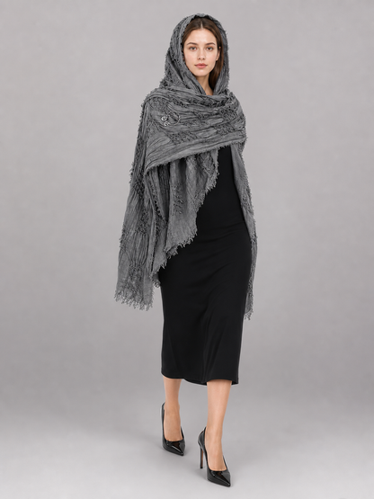 This large scarf-wrap is designed as a rectangular drape with a striking textured surface. The black-and-gray color palette is accented with lighter gray tones, giving the piece a distinctive look that pairs easily with different outfits. T