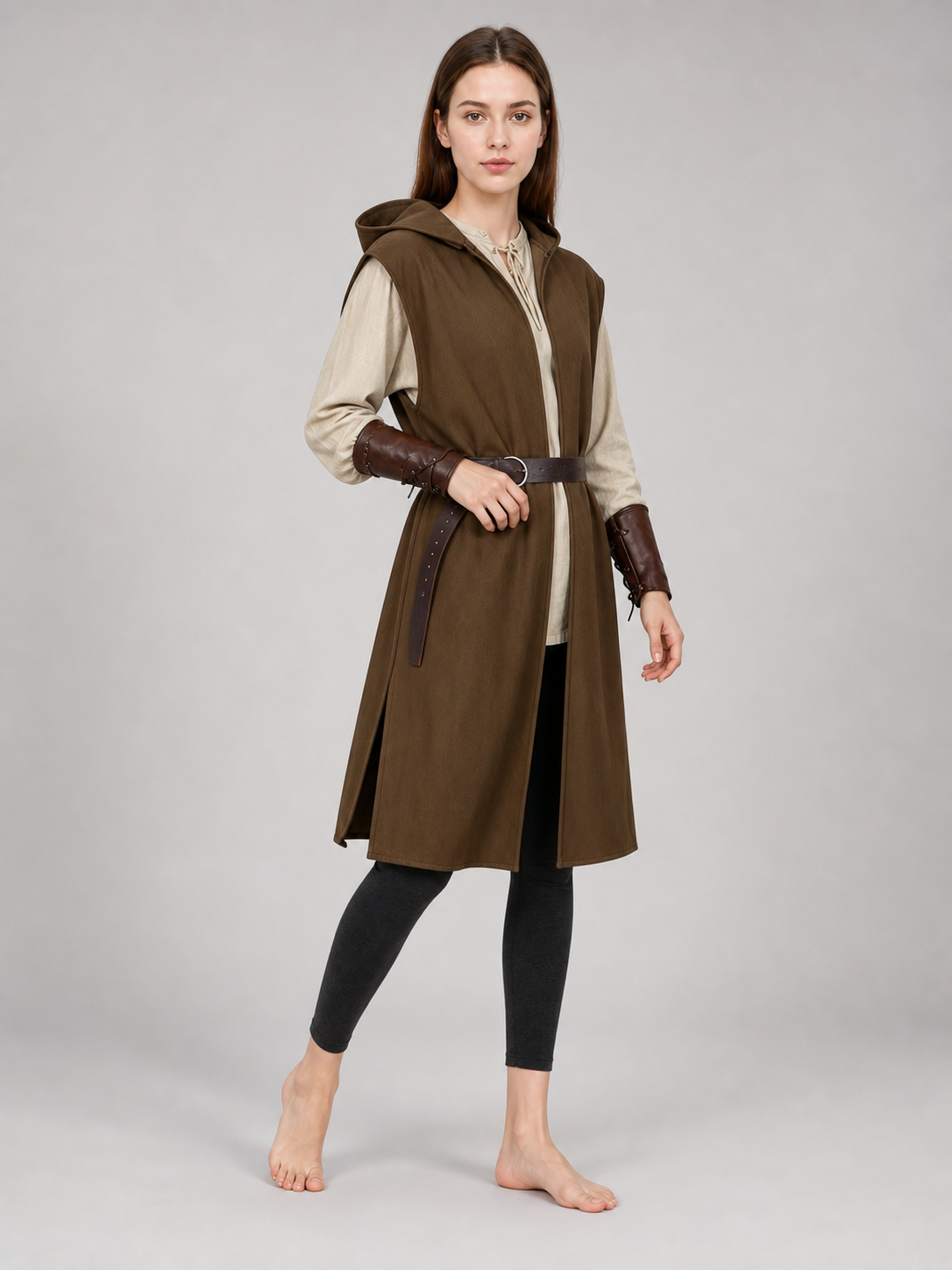 Three-quarter view of a brown hooded vest with a dark belt on a female model, shown over leggings and barefoot