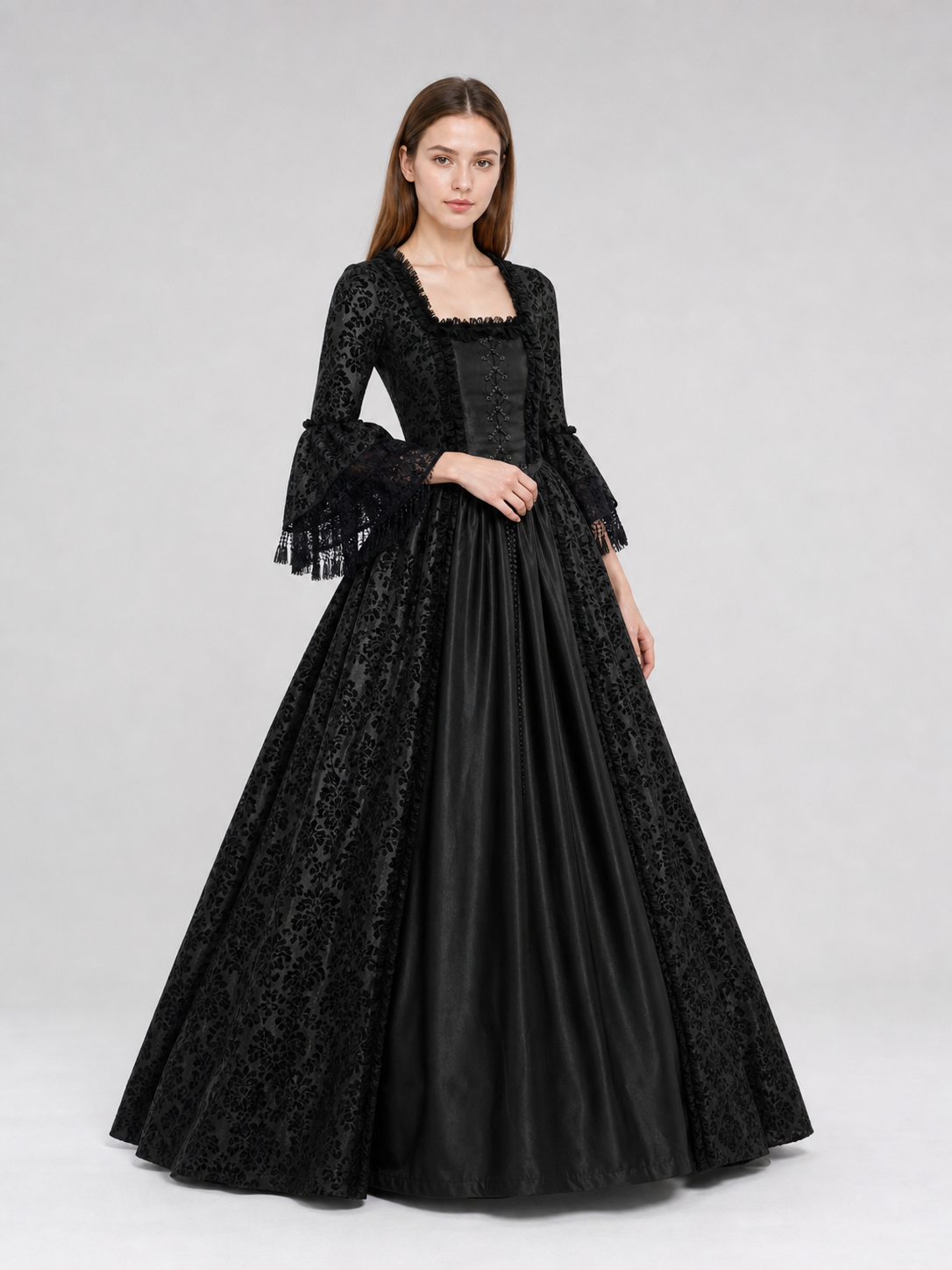 The black dress is designed in the aesthetic of a Victorian-era Gothic costume. The model features a floor-length silhouette, a fitted bodice with a square neckline, and decorative lacing or trim on the front. The long flared sleeves end in