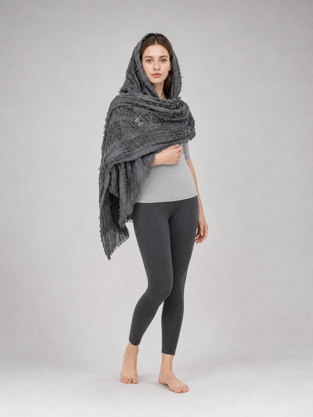 This large scarf-wrap is designed as a rectangular drape with a striking textured surface. The black-and-gray color palette is accented with lighter gray tones, giving the piece a distinctive look that pairs easily with different outfits. T