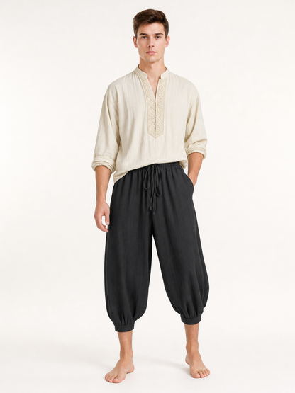 Front view of a man wearing black cropped harem pants with a loose fit, drawstring waistband, side pockets, and gathered cuffs