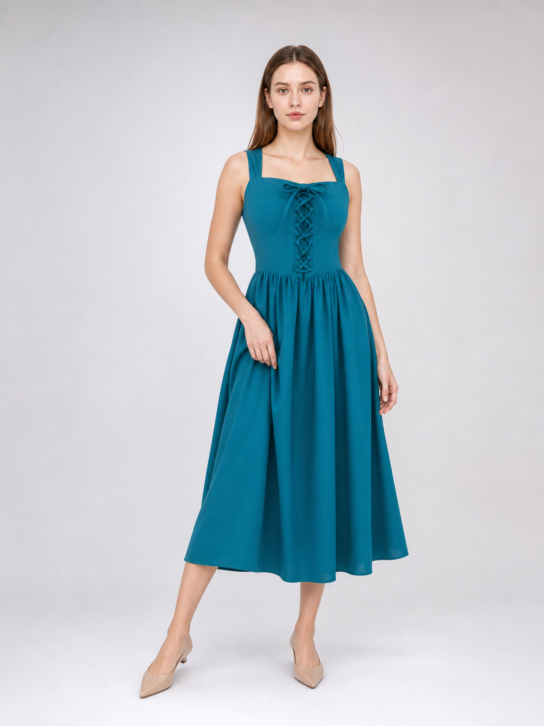 Teal strappy dress with front lacing and a flowing skirt lifted outward by the model in a movement pose
