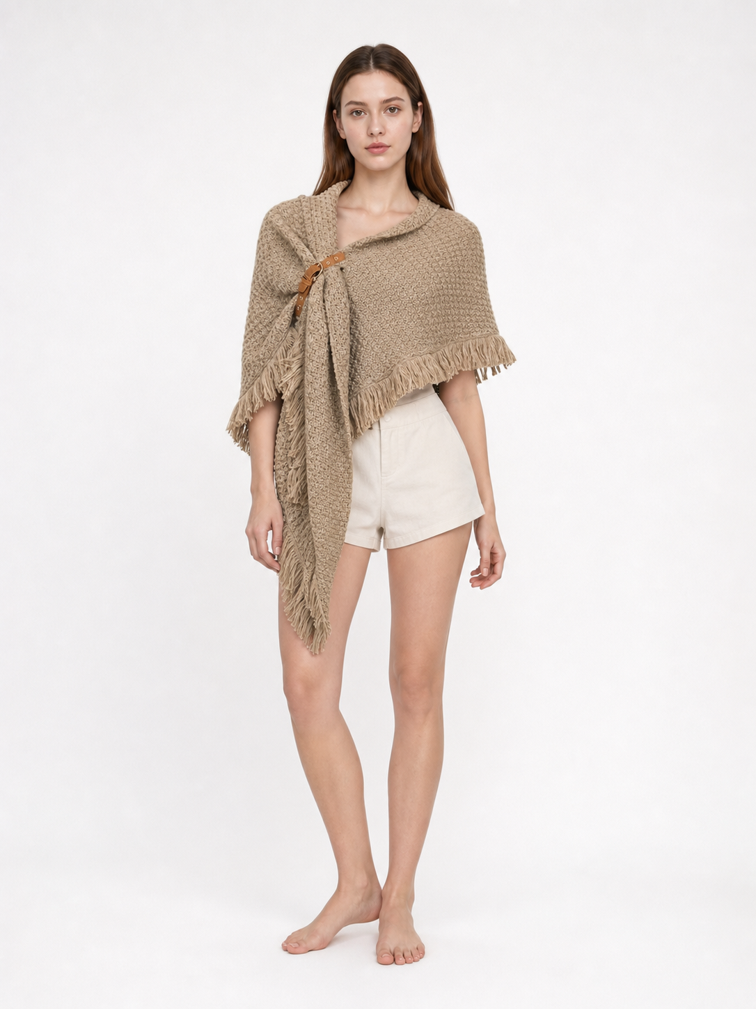 Beige textured cape with a long pointed front and fringe, styled with white shorts on a full-body model