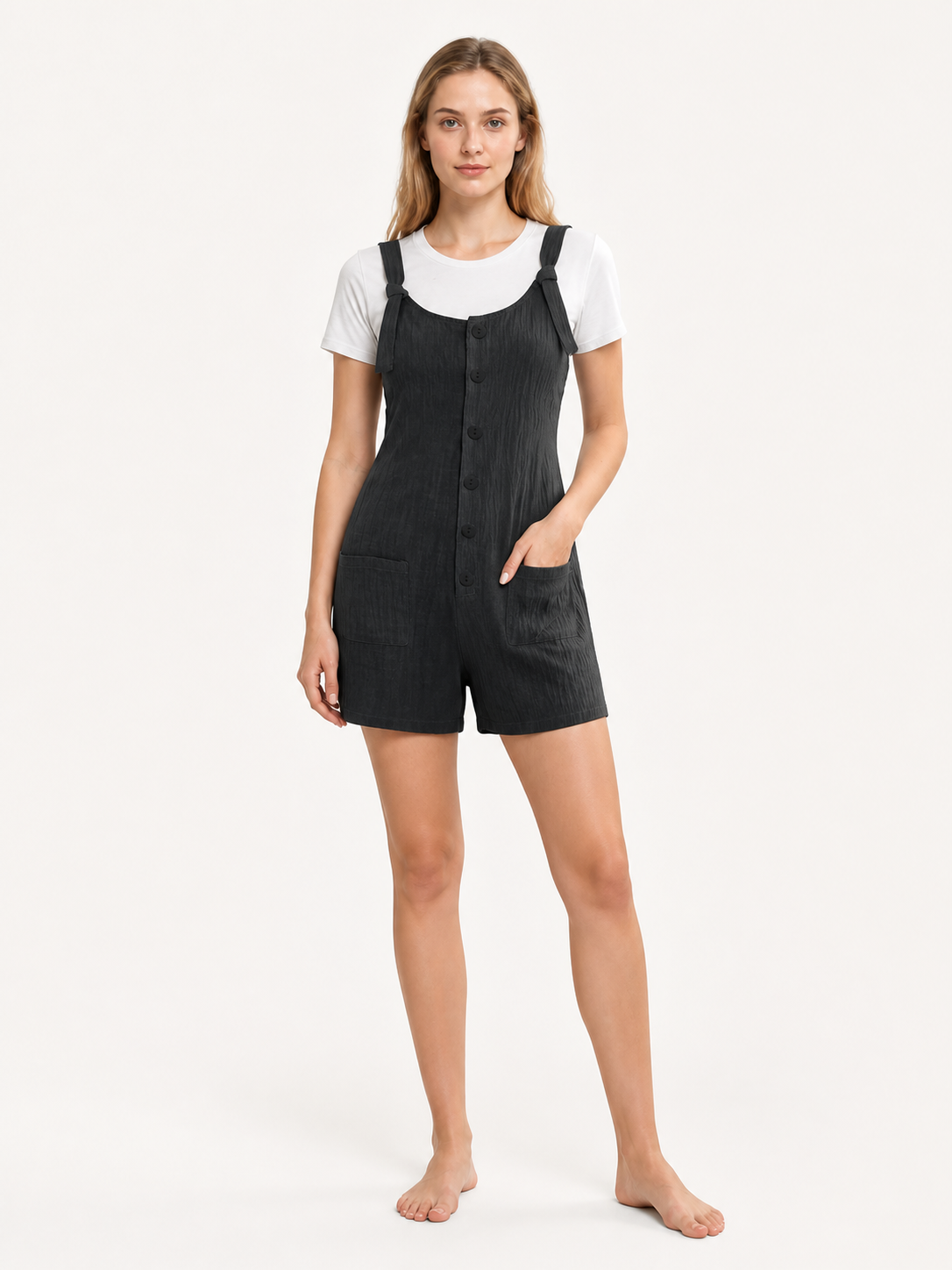 Black textured bib shorts with front buttons and pockets, shown full-body on a barefoot model over a white T-shirt