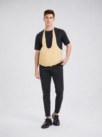 Wearable fake belly costume accessory with a large rounded shape. The model has a bib-style front panel, two shoulder straps, and side ties for fastening. The smooth solid-color surface comes in a light beige or beige shade, so the accessor