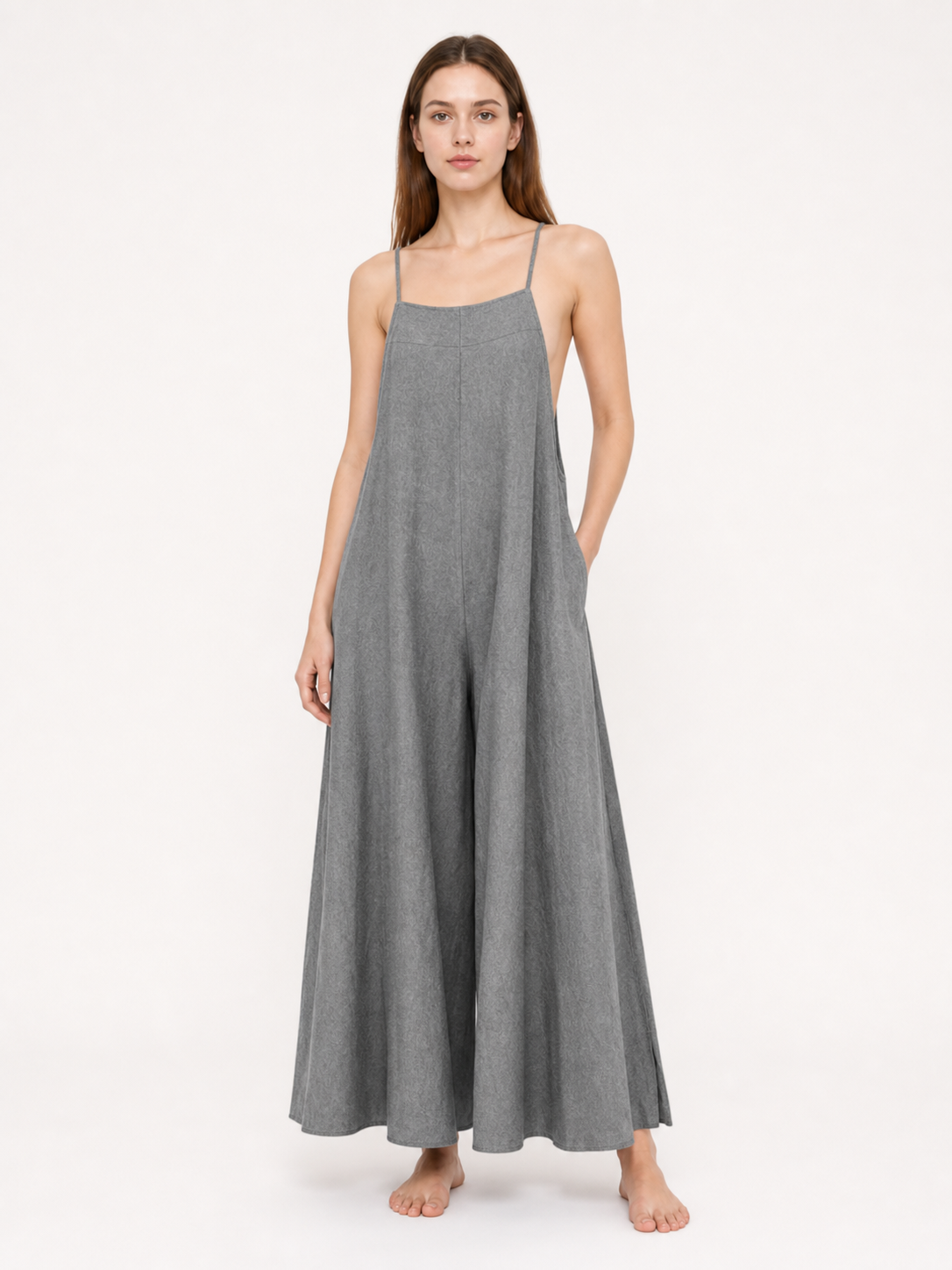 Gray wide-leg jumpsuit with thin straps and side pockets, shown full-length on a model against a pale background