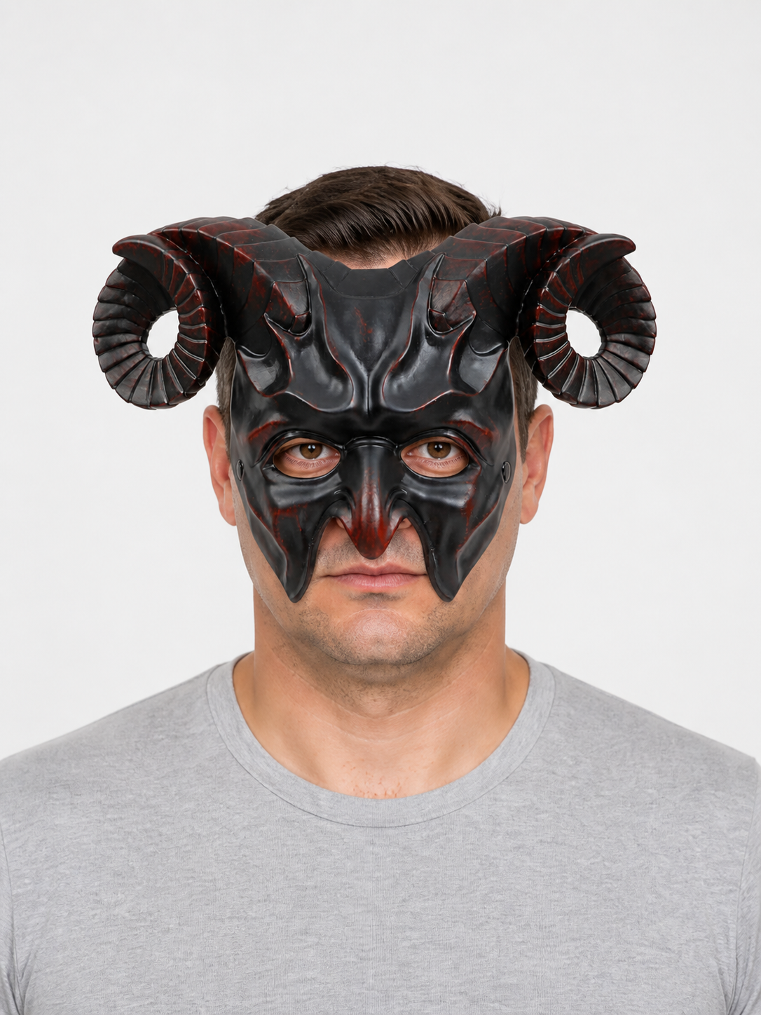 Man wearing a glossy black horned mask with curled ridged horns and pointed facial details against a light gray background