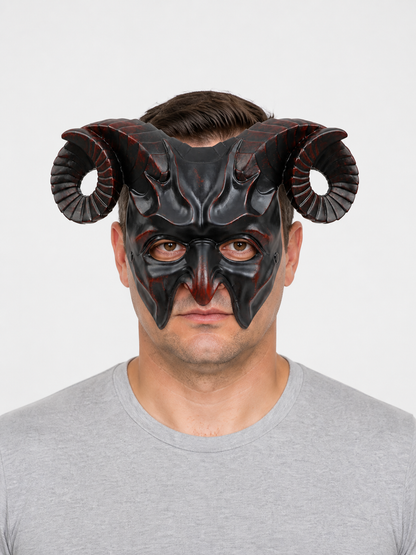Man wearing a glossy black horned mask with curled ridged horns and pointed facial details against a light gray background