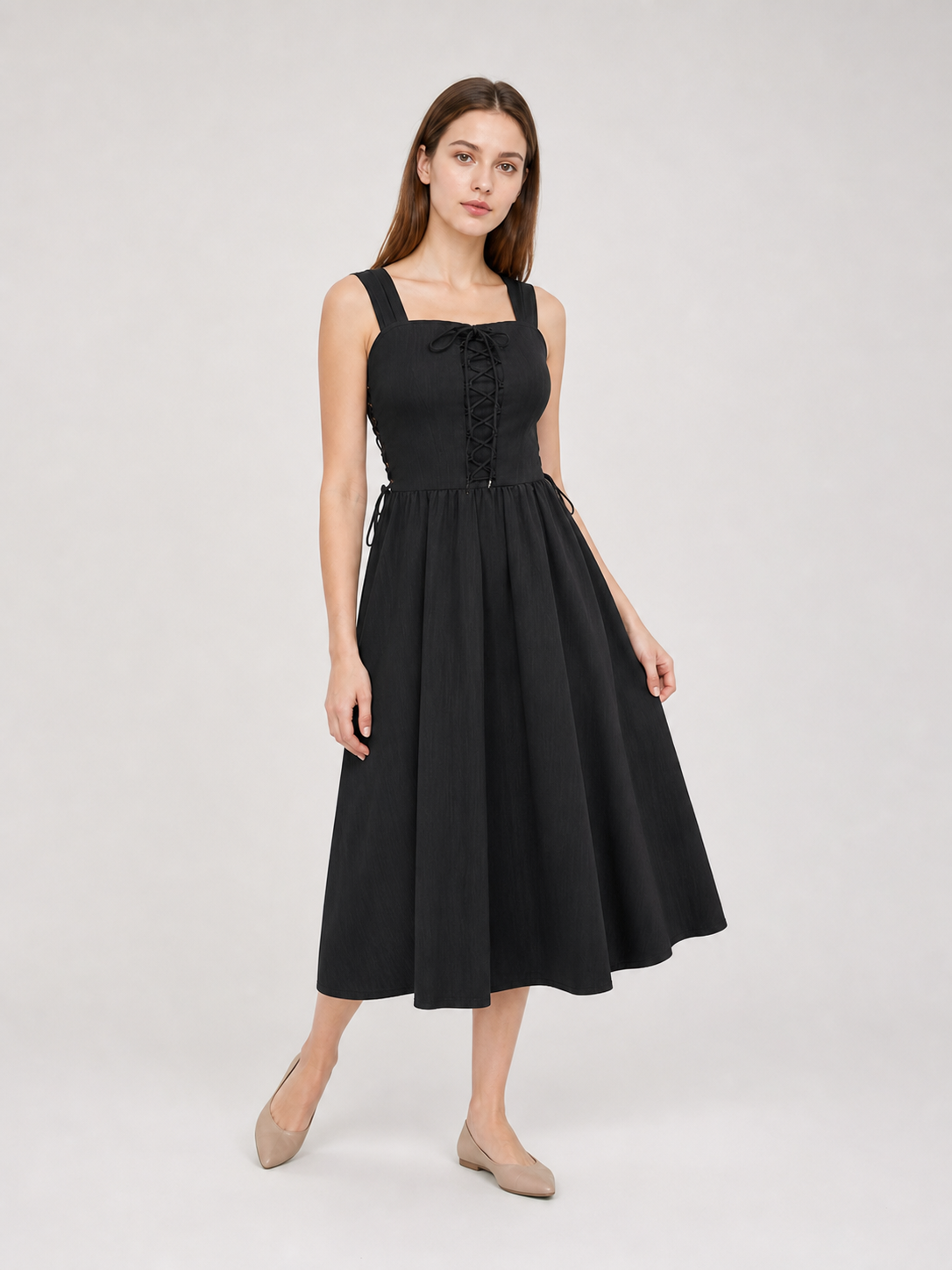 Three-quarter view of a black midi dress on a model, showing the lace-up bodice, side ties, wide straps, and flowing gathered skirt