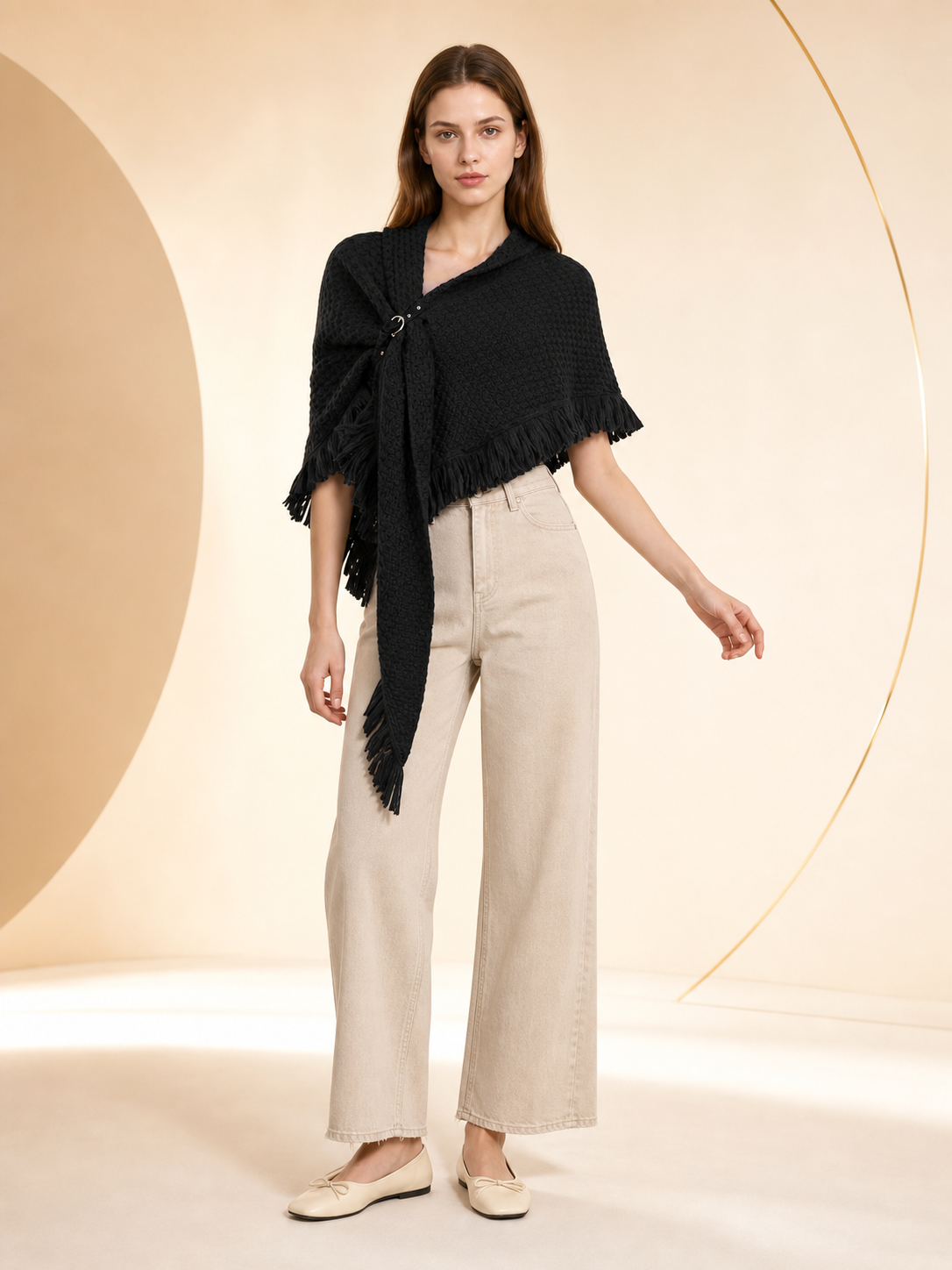 Black knitted poncho cape modeled with beige wide-leg jeans, a long pointed front, fringed edges, and a circular fastening