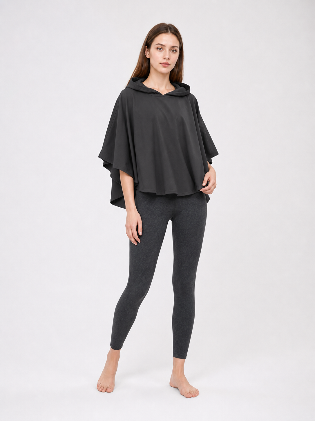 Dark gray hooded poncho with an oversized draped shape, shown from a three-quarter angle on a female model