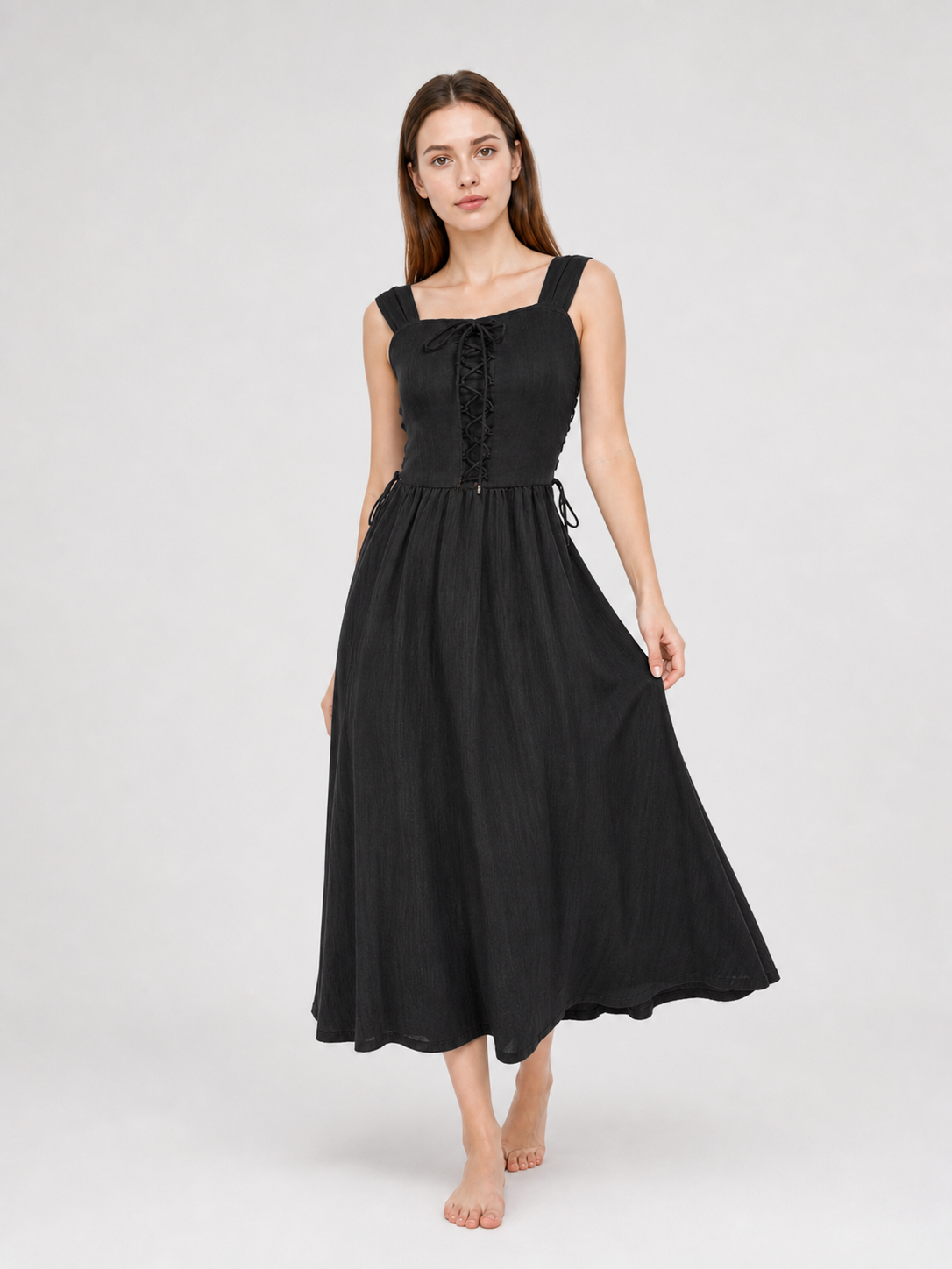 Black midi dress shown in a three-quarter pose on a model, with a lace-up front, broad straps, side ties, and a full mid-calf skirt