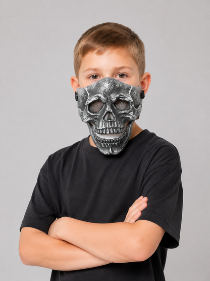 Black skull face mask with hollow eye openings and layered molded teeth, shown front-facing on a child with folded arms
