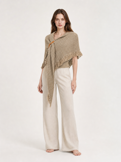 Back view of a beige woven cape on a model wearing black leggings, showing the triangular drape and fringed hem