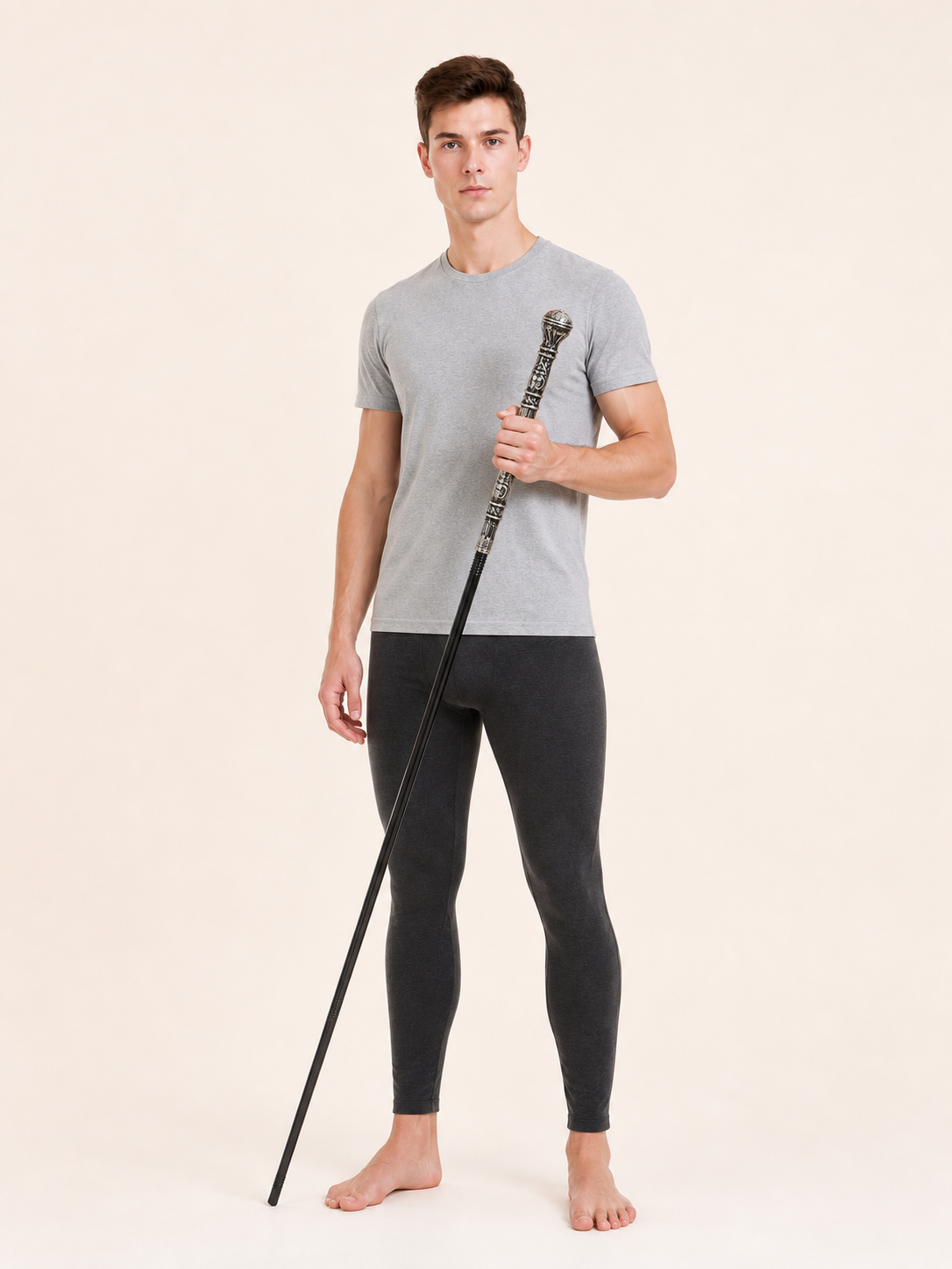 Front view of a man in a gray shirt and dark leggings holding the black cane upright against a light background