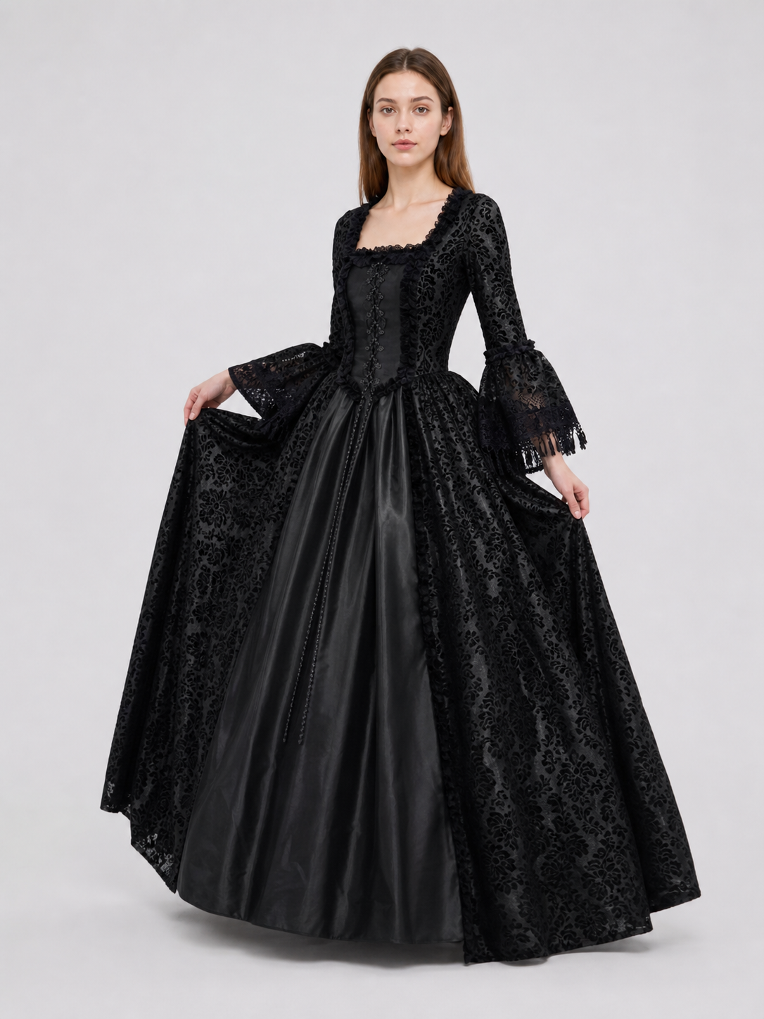 The black dress is designed in the aesthetic of a Victorian-era Gothic costume. The model features a floor-length silhouette, a fitted bodice with a square neckline, and decorative lacing or trim on the front. The long flared sleeves end in