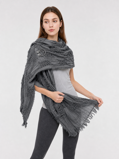 This large scarf-wrap is designed as a rectangular drape with a striking textured surface. The black-and-gray color palette is accented with lighter gray tones, giving the piece a distinctive look that pairs easily with different outfits. T
