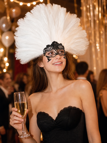 White feather headpiece with a black lace mask, shown on a smiling model in a black dress holding a champagne flute