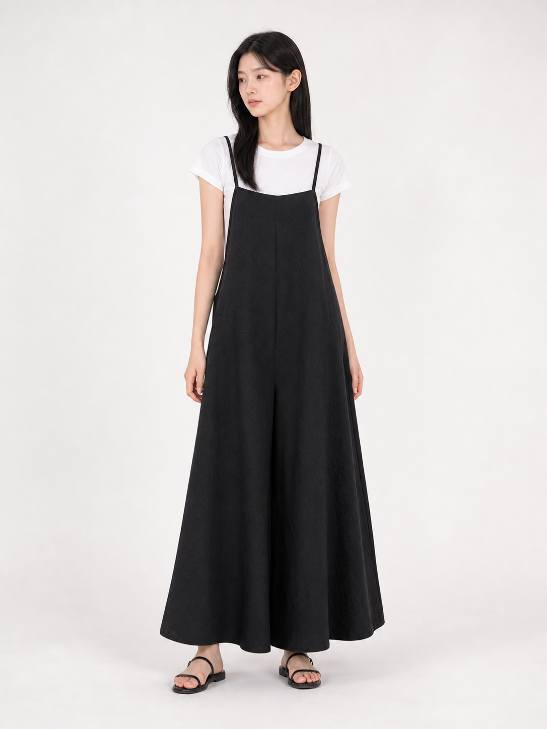 Black wide-leg jumpsuit layered over a white short-sleeve shirt, shown full-body on a model wearing flat sandals