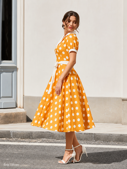 Dress with a White Collar, Bow Belt, and Polka-Dot Print. The dress is designed in an orange-and-white color scheme, with a white polka-dot pattern on an orange background across the upper portion and skirt. A white Peter Pan collar and sho