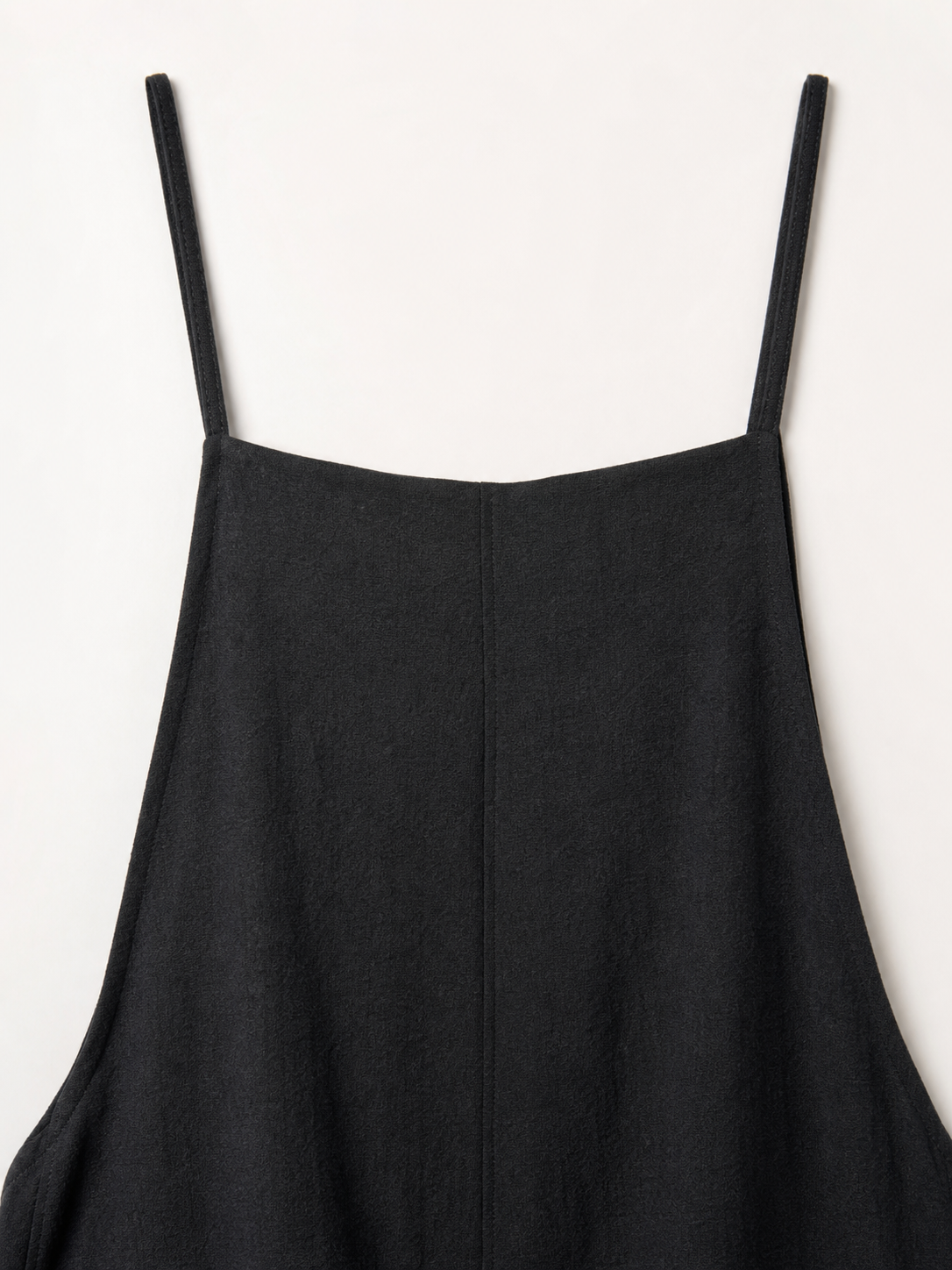 Loose black bib overalls with thin shoulder straps. The design features a simple solid black color and a straight, wide-leg silhouette with long pant legs. The upper portion is styled as a bib, while the thin shoulder straps complement the 